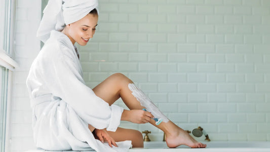A woman in a bathrobe relaxes on the edge of a bathtub, surrounded by Tend Skin products for skincare.